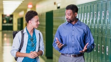 Teacher and student talking in a school hallway.
