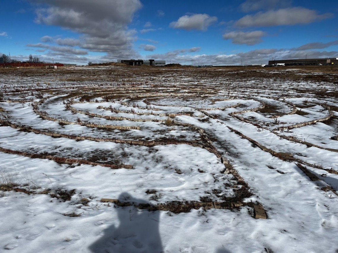 A photograph of the snowy ground in a wide open field shows the outlines of an outdoor maze at William Smith High School