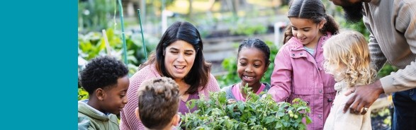 Two adults with a group of children learning at a community garden