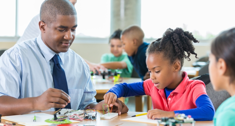 African American man teaching elementary school students about robotics stock