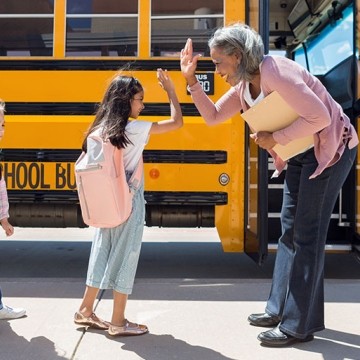Adult and student high-fiving in front of a school buss