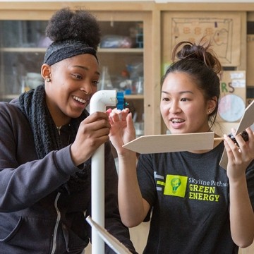 Three high school students stand and work together on building a windmill for a  science project.