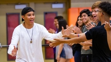 Young man giving high fives to high school age youth.