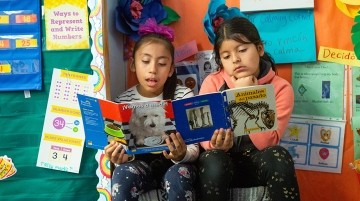 Two elementary girls reading Spanish language books.