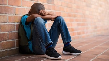 Elementary school boy seated on the floor with head down.