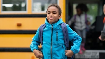 Elementary school boy getting off a yellow school bus.