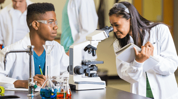 Teacher checking the microscope of a student in a science lab.