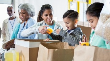 Adults and children filling brown bags with food items.