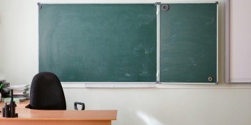 The front of an empty classroom, with a teacher's desk and a chalkboard wiped clean