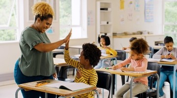 A teacher giving a student a high five in a classroom.