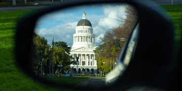 A photo of the California State Capitol building in the sideview mirror of a car.