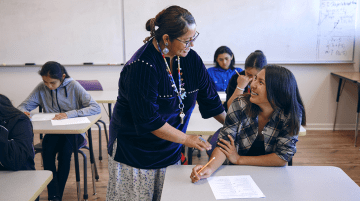 A teacher speaking with a student in a classroom.