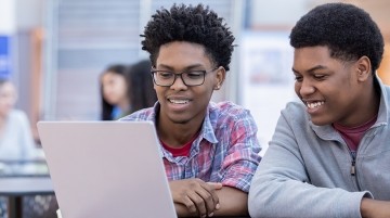 Two high school students working together on a laptop.