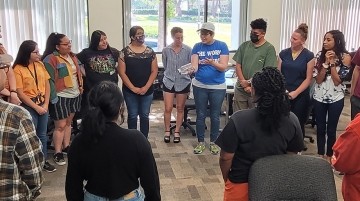 A group of adults standing a circle while having a discussion.