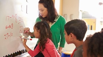 A teacher assisting students with a math equation on a whiteboard.