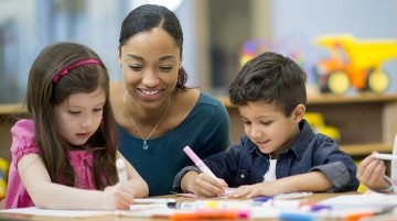 A teacher assists preschool students with a task.
