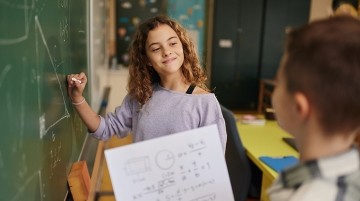 Two students solving a math equation on a blackboard.