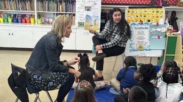 Two teachers reading a book to a group of kindergarteners.