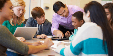 Group of students and a teacher in discussion around a table