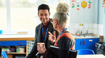 Two teachers having a discussion in a classroom.
