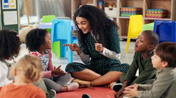 A teacher and elementary students seated on a rug in a classroom.