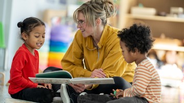 A teacher reads a book to two PreK students.