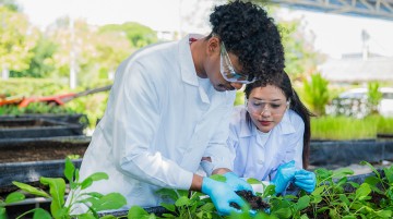 Two high school students wearing lab coats in a plant nursery.