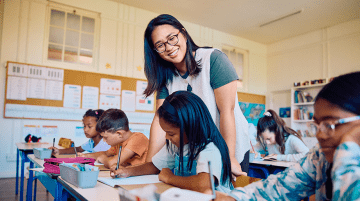 A teacher assists an elementary student with an assignment in a classroom.