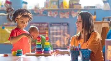 A teacher assists a preschool student with a stacking toy.