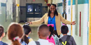 A school leader welcomes children in a hallway.