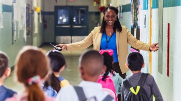 An educator smiles in front of a group of students in a school hallway.