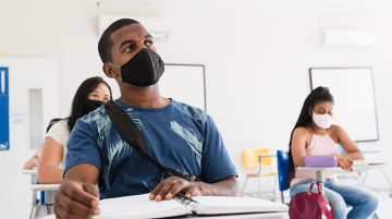 Young adults wearing masks and seated in a classroom.