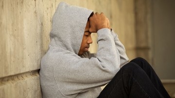 Teenage boy sitting on floor with this arms covering his face