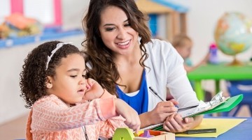 Woman with a clipboard observing a young girl in a school setting