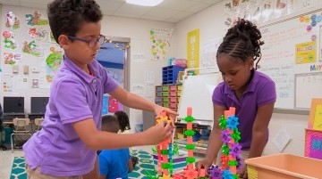 Two students work on building a structure out of colorful blocks