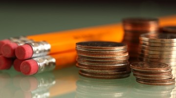 Yellow pencils and stacked coins on a reflective surface.