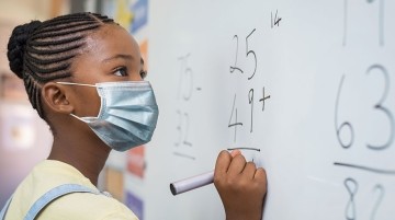 African American student wearing a mask and writing on a whiteboard.