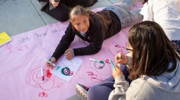 Classmates drawing with markers outdoors.