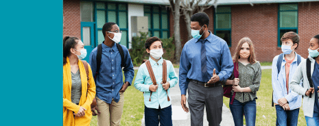 Male teacher and students wearing masks while having a discussion outdoors