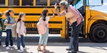 Principal giving a student a high five in front of a parked bus.