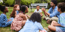 Teacher talking with young students while seated on the grass.