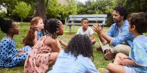 Teacher sitting with young students on lawn by a bench 