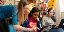 A teacher helping a student on a laptop.