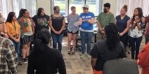 A group of adults standing a circle while having a discussion.