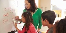 A teacher assisting students with a math equation on a whiteboard.