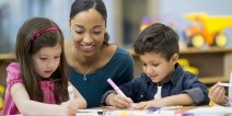 A teacher assists preschool students with a task.