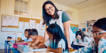 A teacher assists an elementary student with an assignment in a classroom.