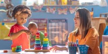A teacher assists a preschool student with a stacking toy.