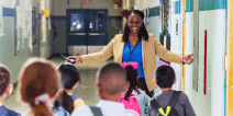 A school leader welcomes children in a hallway.