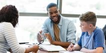 Two adults assist a student with an assignment in a classroom.